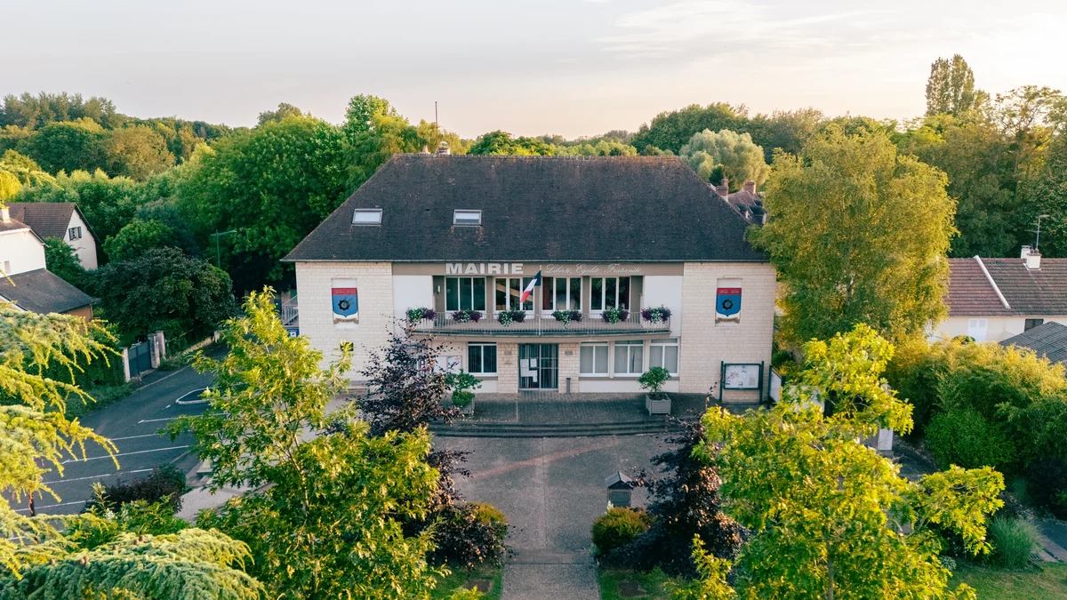 Façade de la mairie de Giberville photographiée depuis les airs, entre les arbres.
