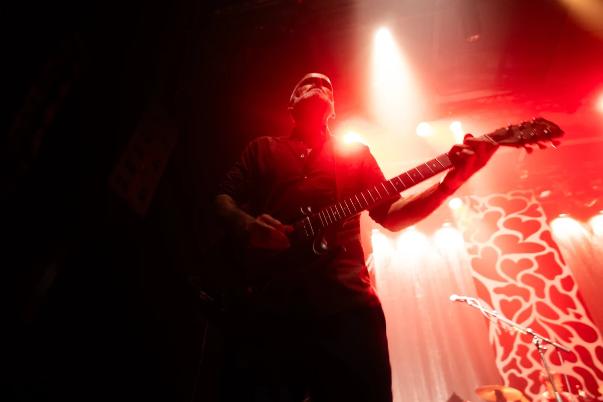 Un guitariste de La Maison Tellier photographié en contre-plongée dans un éclairage rouge.