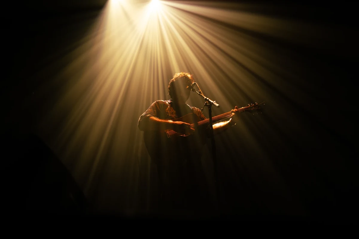 Un chanteur de La Maison Tellier joue de la guitare acoustique sous un faisceau de lumière dorée.