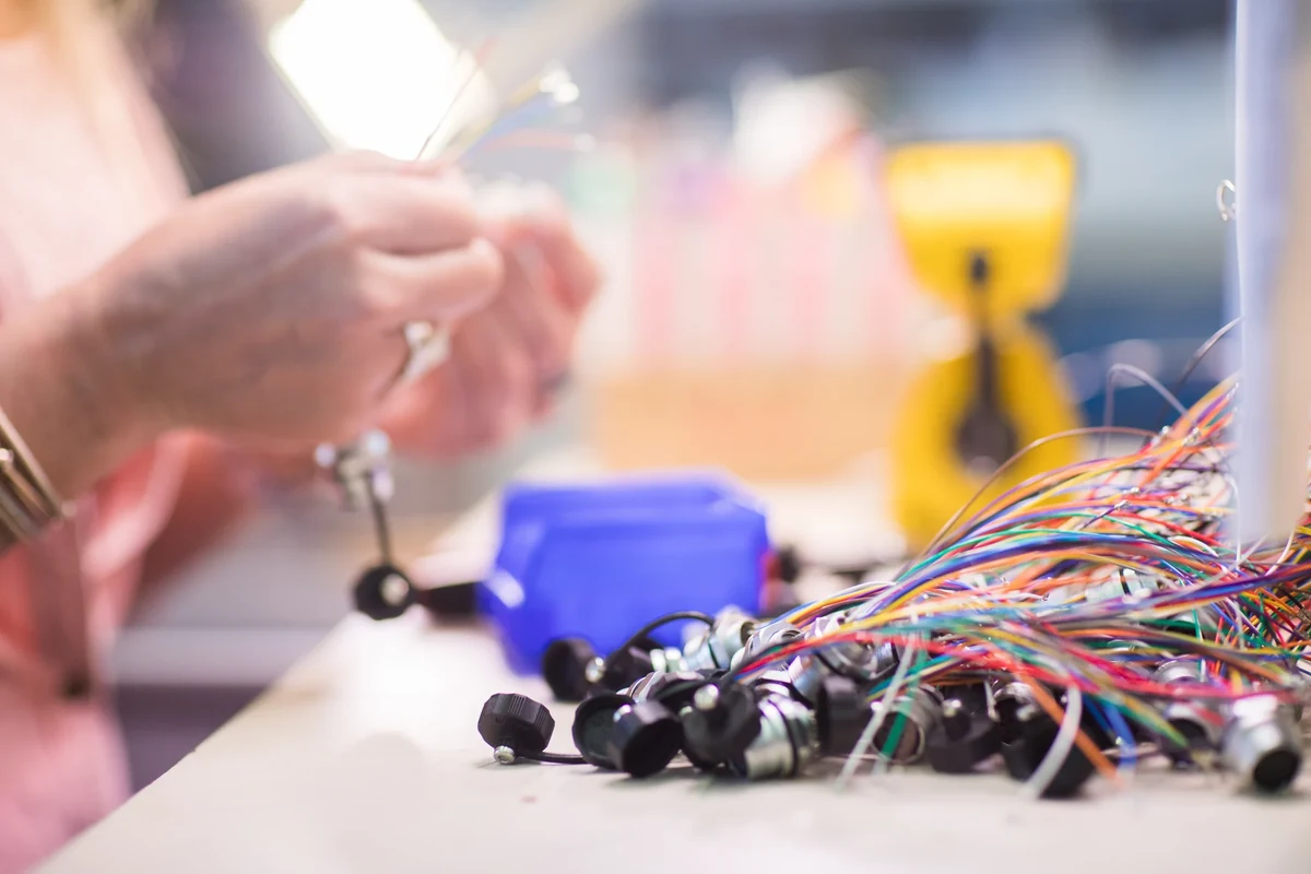 Mains au travail au-dessus de câbles multicolores sur un établi.