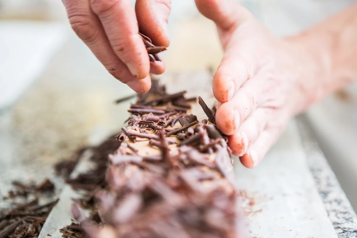 Mains déposant des copeaux de chocolat sur une pâtisserie.