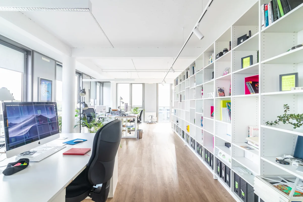 Bureaux lumineux d’Unik Studio avec postes de travail et longue bibliothèque blanche.