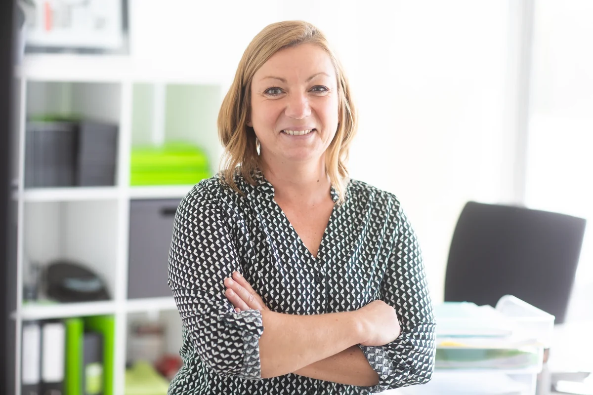 Portrait d’une femme souriante, les bras croisés, dans les bureaux d’Unik Studio.